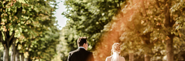 Ein Brautpaar läuft eine Allee entlang von der Kamera weg